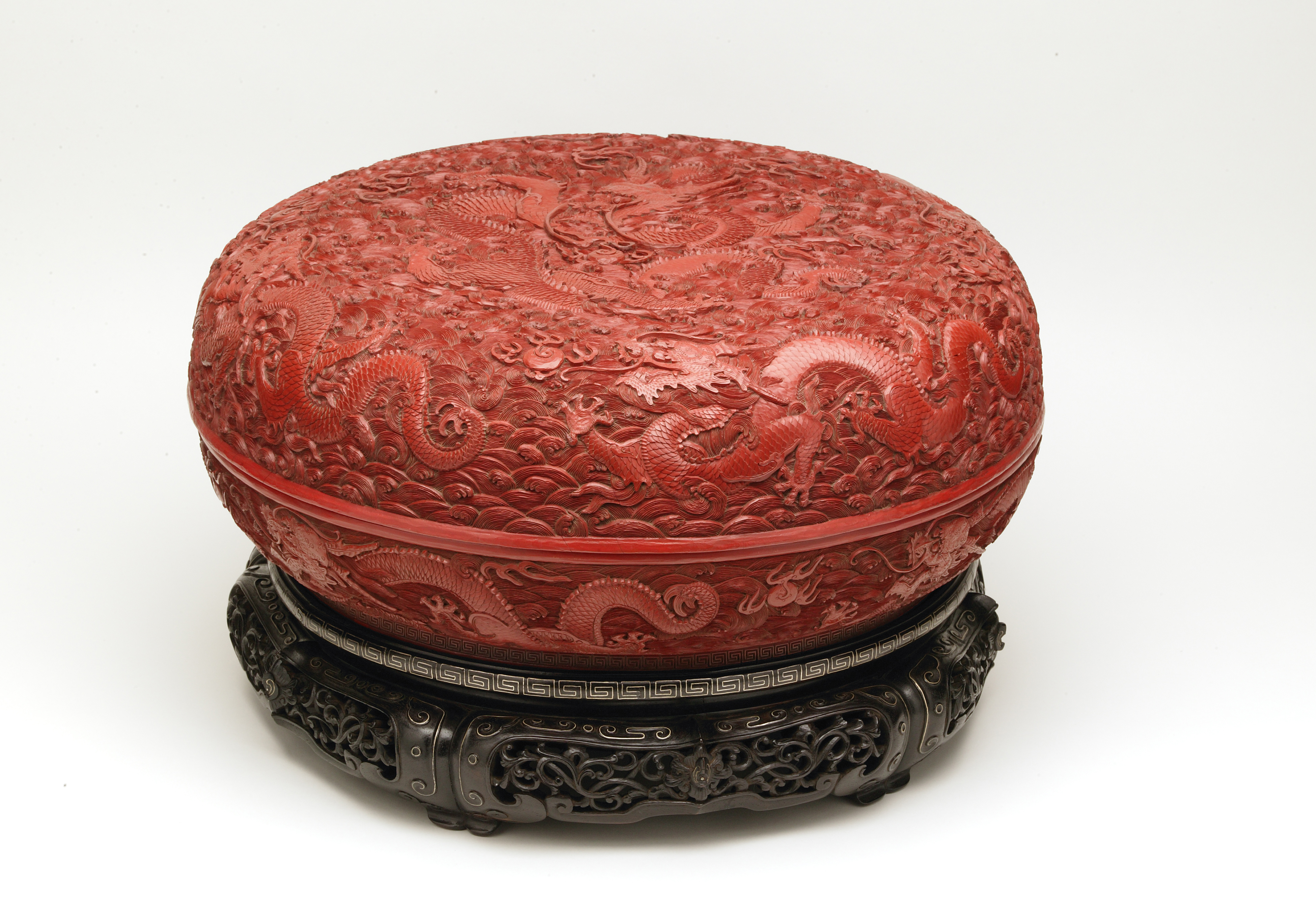 A single object image of a red lacquer box with dragon motifs on a wooden base.